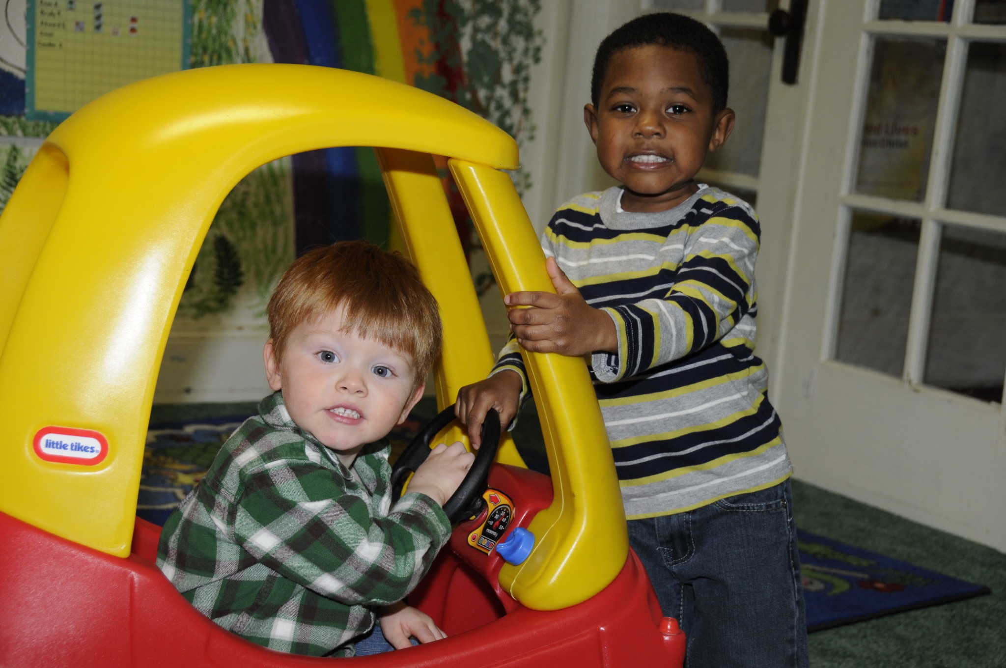 Two young children playing together with a toy car during a church activity