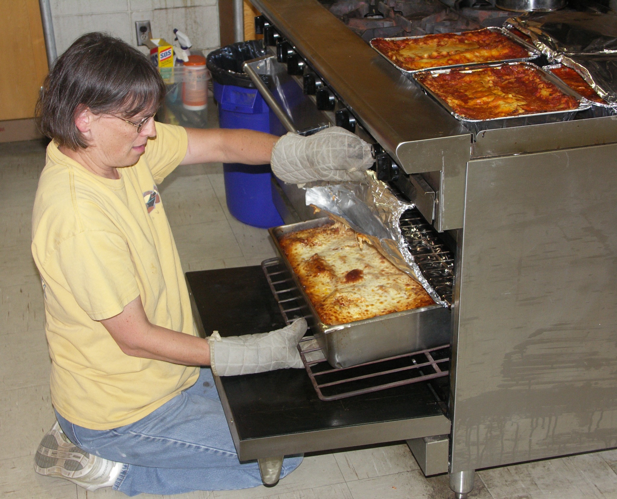 A church volunteer preparing pans of food in the kitchen for a community dinner.