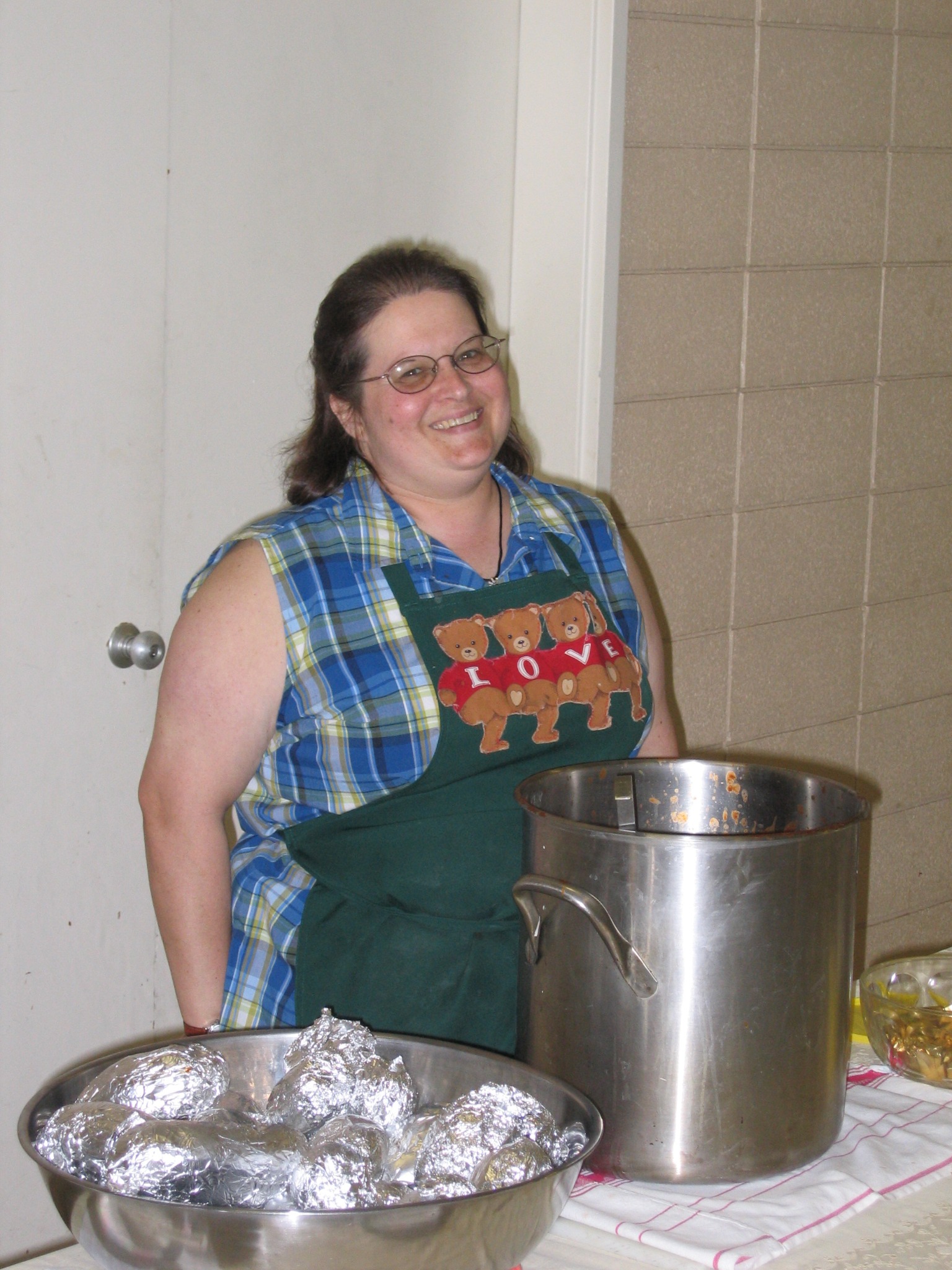 A woman standing beside a large pot of food prepared for a church community dinner.